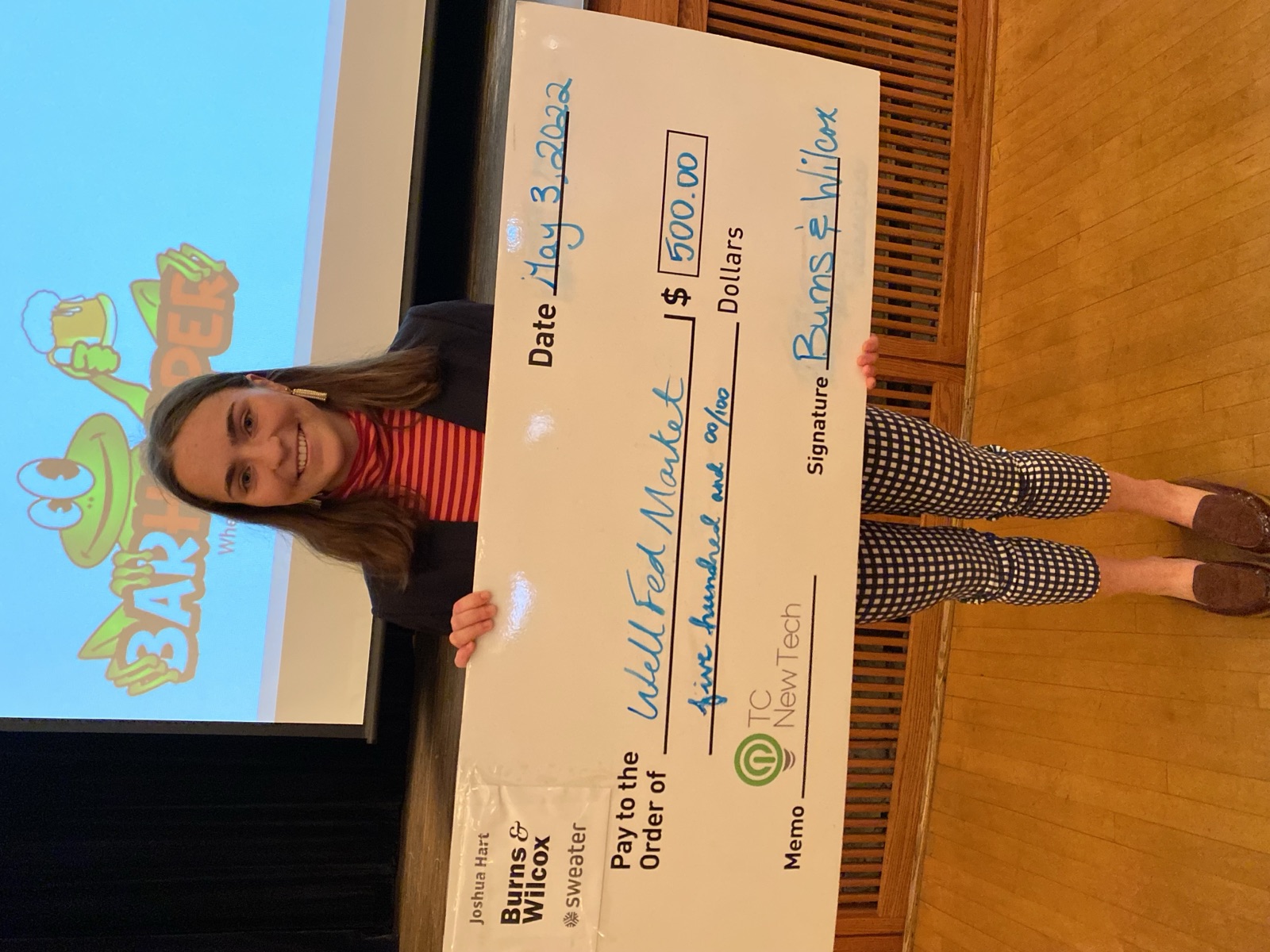 Elizabeth Saunders holding the Wellfed Market funding check on stage at TCNewTech